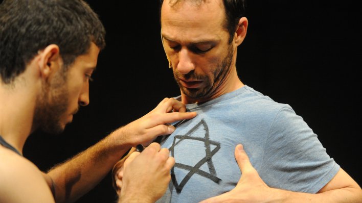 A dancer draws the Star of David onto the chest of the other dancer.