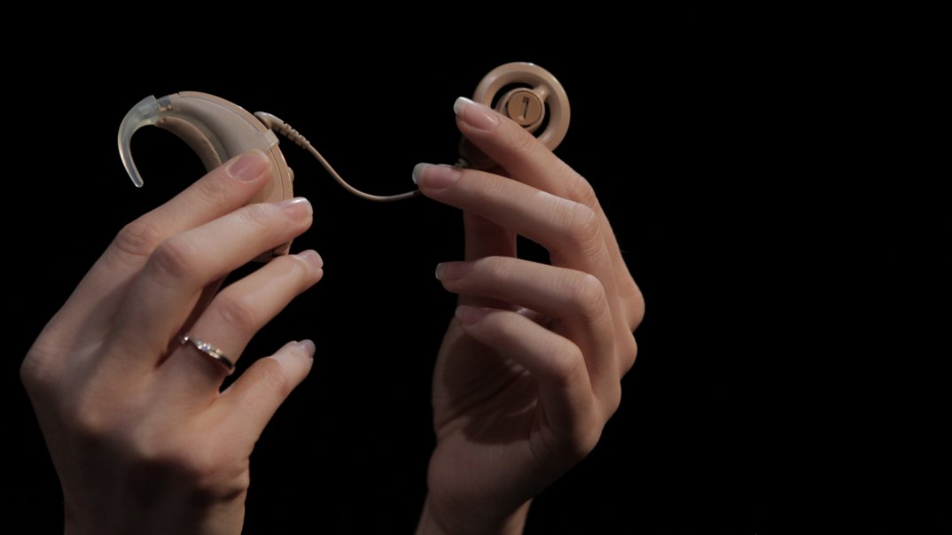 zwei Frauenhände halten ein beiges Cochlea-Implantat hoch.
