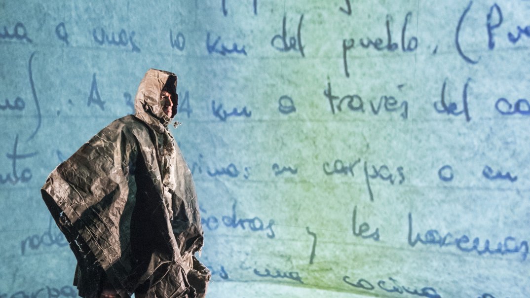 Ein Soldat aus Campo Minado/Minefield steht in Regenjacke vor projiziertem spanischen Text