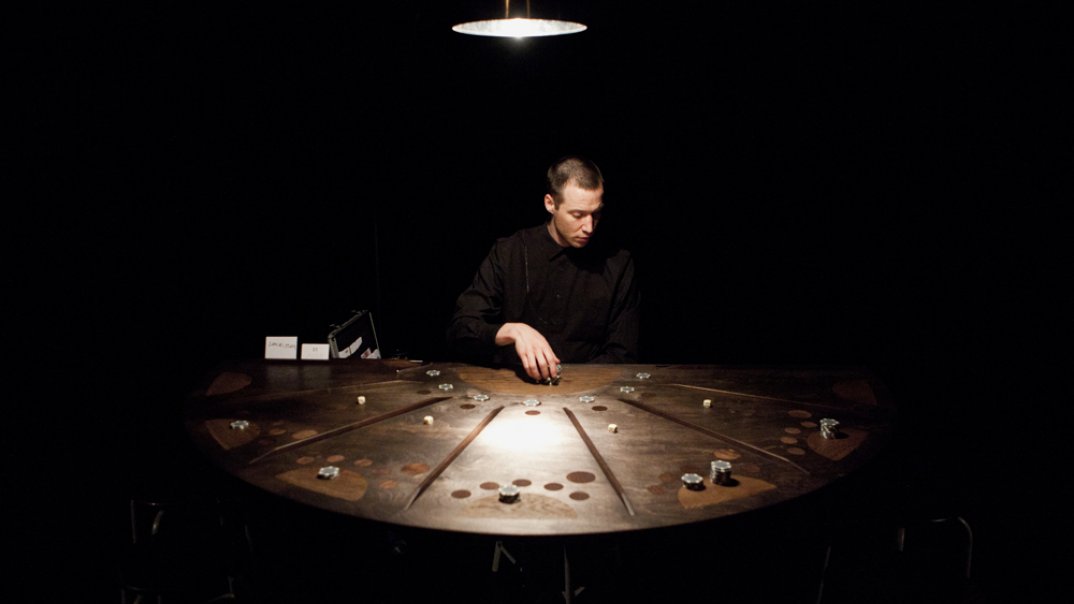 Der Croupier sitzt allein am Spieltisch in der Halbkreis-Form und sortiert die Münzen aus.