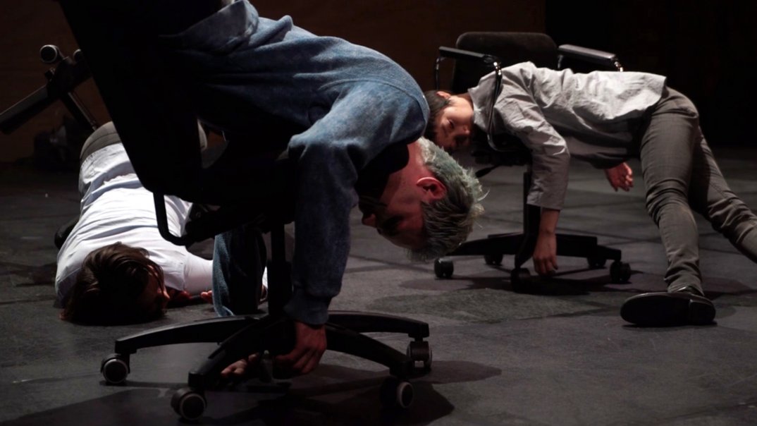 two men are romping around chairs.