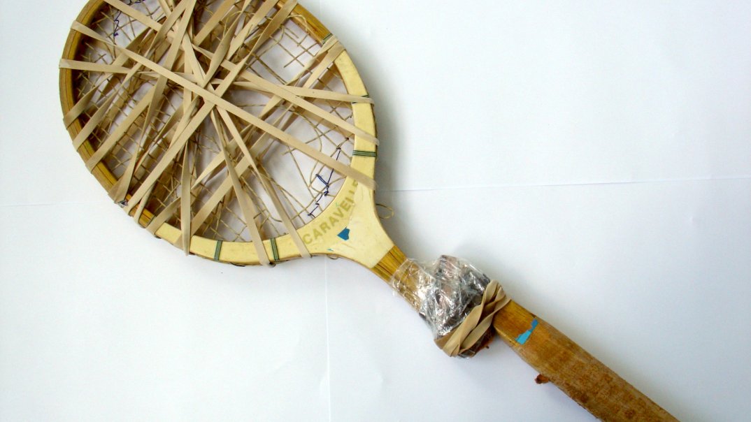 Ein alter Tennisschläger wird zu einem Kunstwerk verarbeitet. Die Draht der Tennisschläger sind aufgelöst und es wird deswegen mit Klebbanden übergedeckt.